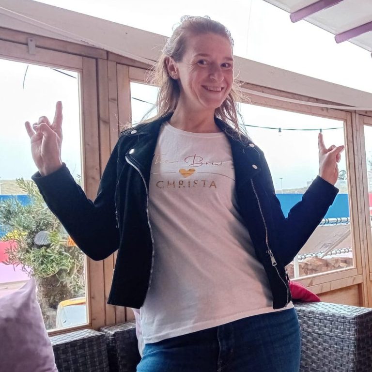 Christa met een witte T-shirt en zwarte leren jas, maakt rockhandgebaren.